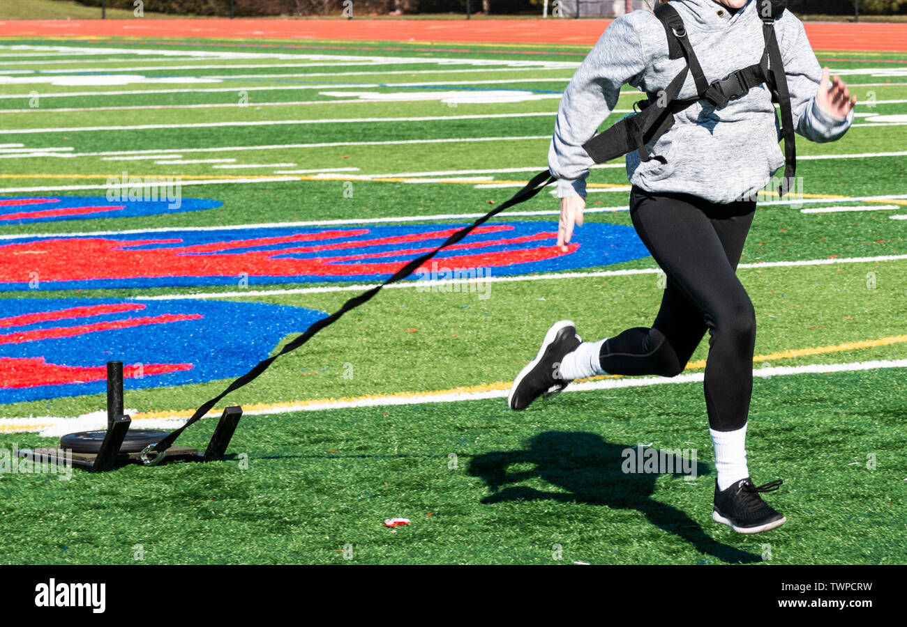 High school runner is pulling a sled with weight across a green turf