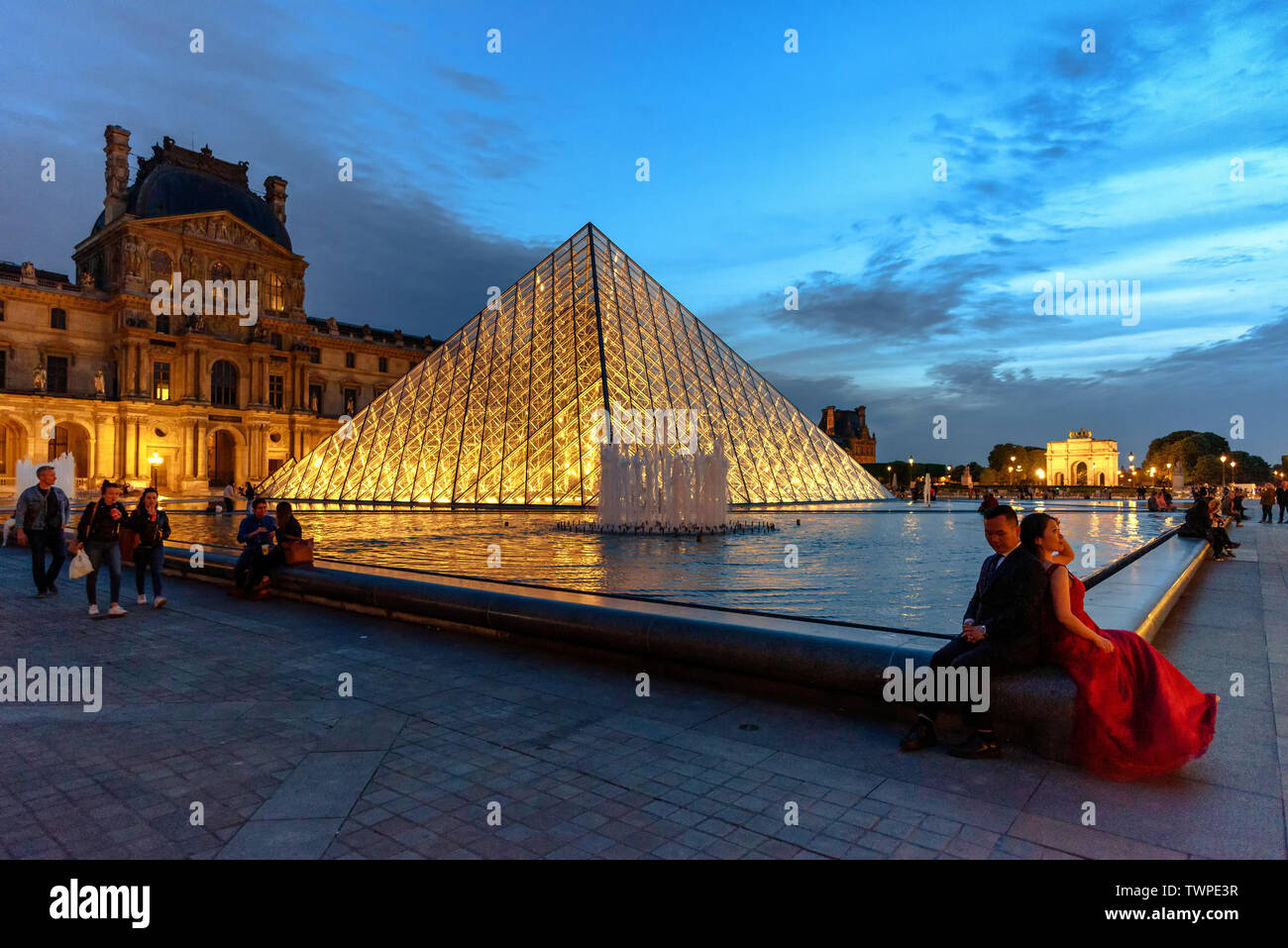 A couple taking engagement photos by the illuminated glass pyramid at ...