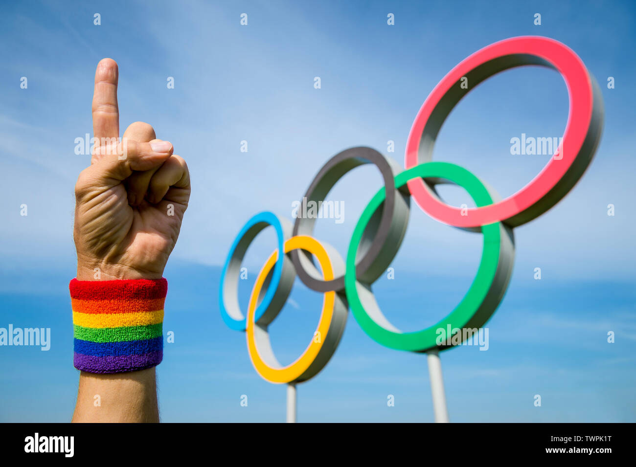 LONDON - MAY 4, 2019: A hand wearing gay pride rainbow colored wristband points to the sky with a number one gesture in front of Olympic Rings. Stock Photo