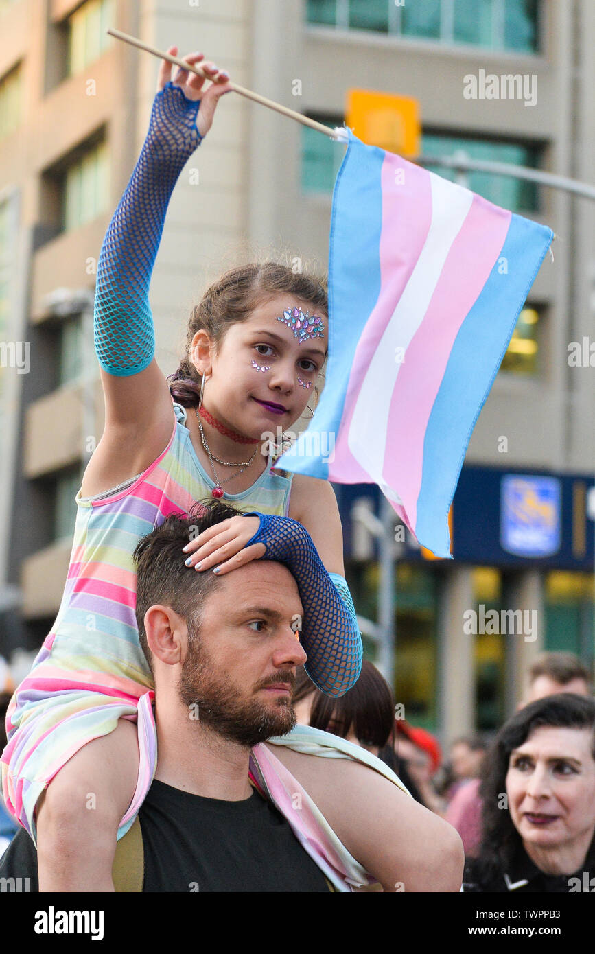 A girl on top of a man's shoulders holds a flag during the Trans march.Spectators displayed their support towards the transgender and non-binary people while demonstrating on the streets of Toronto in a Trans March during the Pride Month. Stock Photo