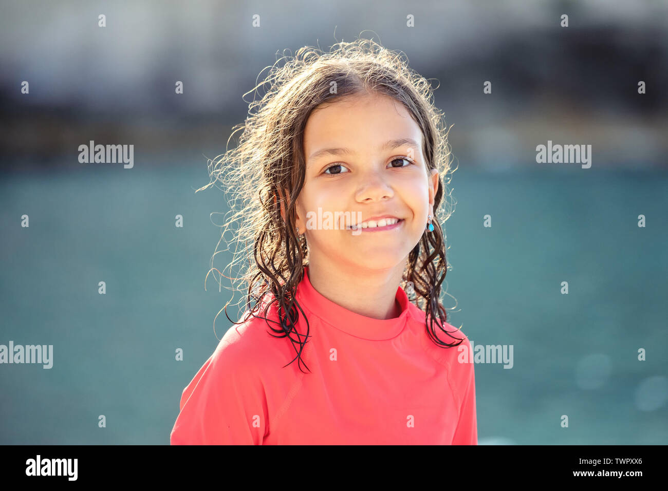 Beautiful little girl with wet hair smiling and looking at camera at beach during sunset - Outdoor portrait of happy child - cheerful kid laughing Stock Photo