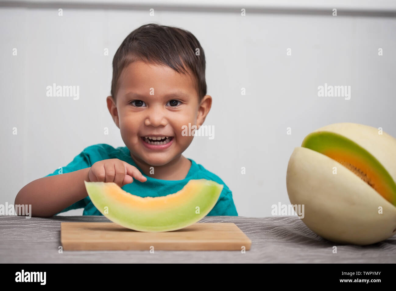 A happy young kid with cute smile points to his slice of a honeydew melon he is about to eat as part of a healthy snack. Stock Photo