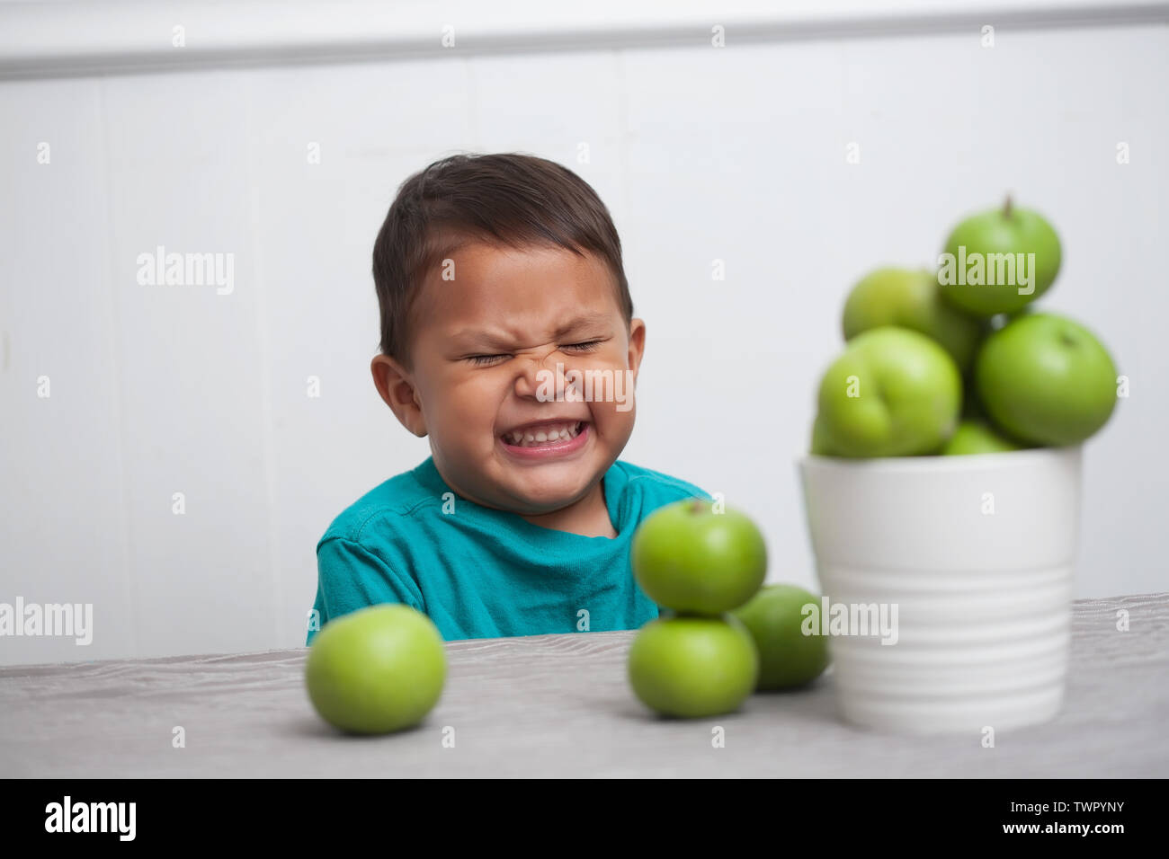 Young boy cheerfully grinning and sitting in front of a bunch of green apples. Stock Photo