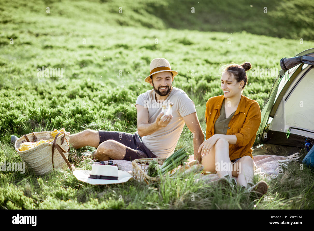 Young and cheerful couple having a picnic at the campsite while traveling high in the mountains during the sunset Stock Photo