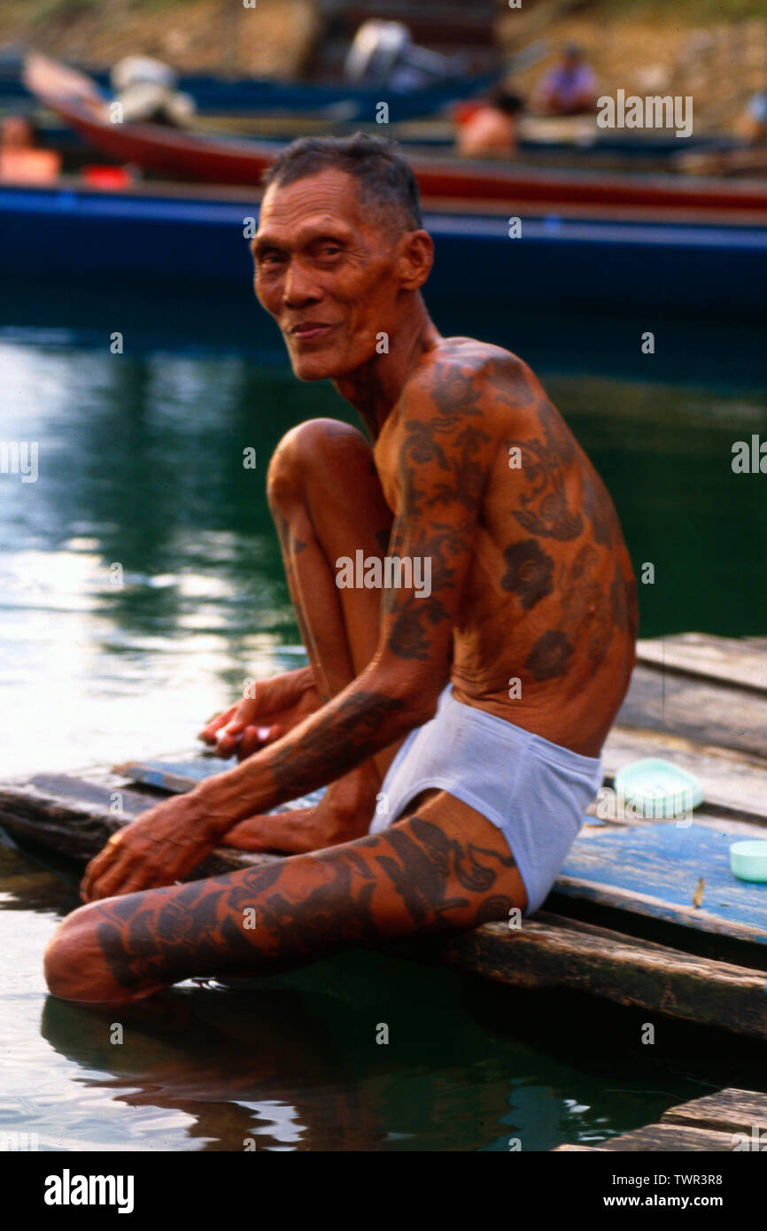 Malaysia/Borneo: Older Iban Headhunter with tatoo's at the river  sitting in the rain forest of Sarawak Stock Photo