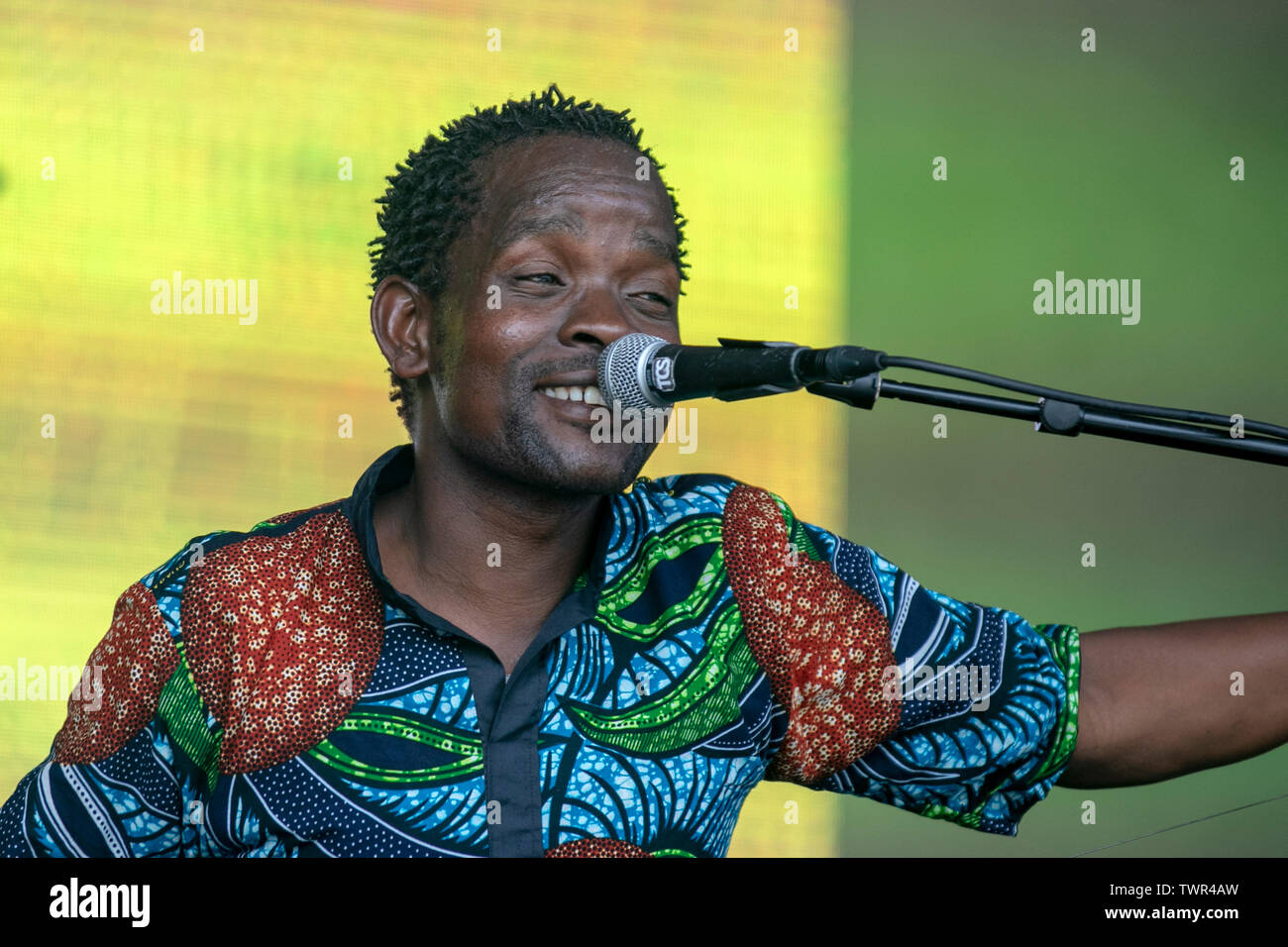 Gasper Nali singing entertains the crowds in Sefton Park at the Liverpool Africa Oye event. Gasper Nali is a Malawi Kwela roots musician from Nkhata on the shores of Lake Malawi.He plays a one-string bass guitar with a stick and an empty beer bottle, along with a cow skin kick drum. Stock Photo