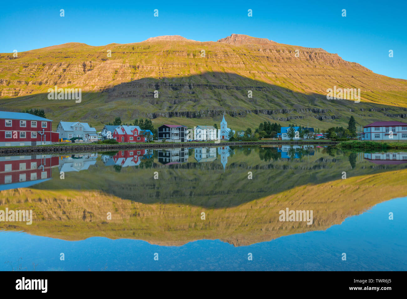Perfect water reflection, perfect mirrored image of an Icelandic fjord town in the water, sunrise reflection with perfect mountain shadow in the fjord Stock Photo