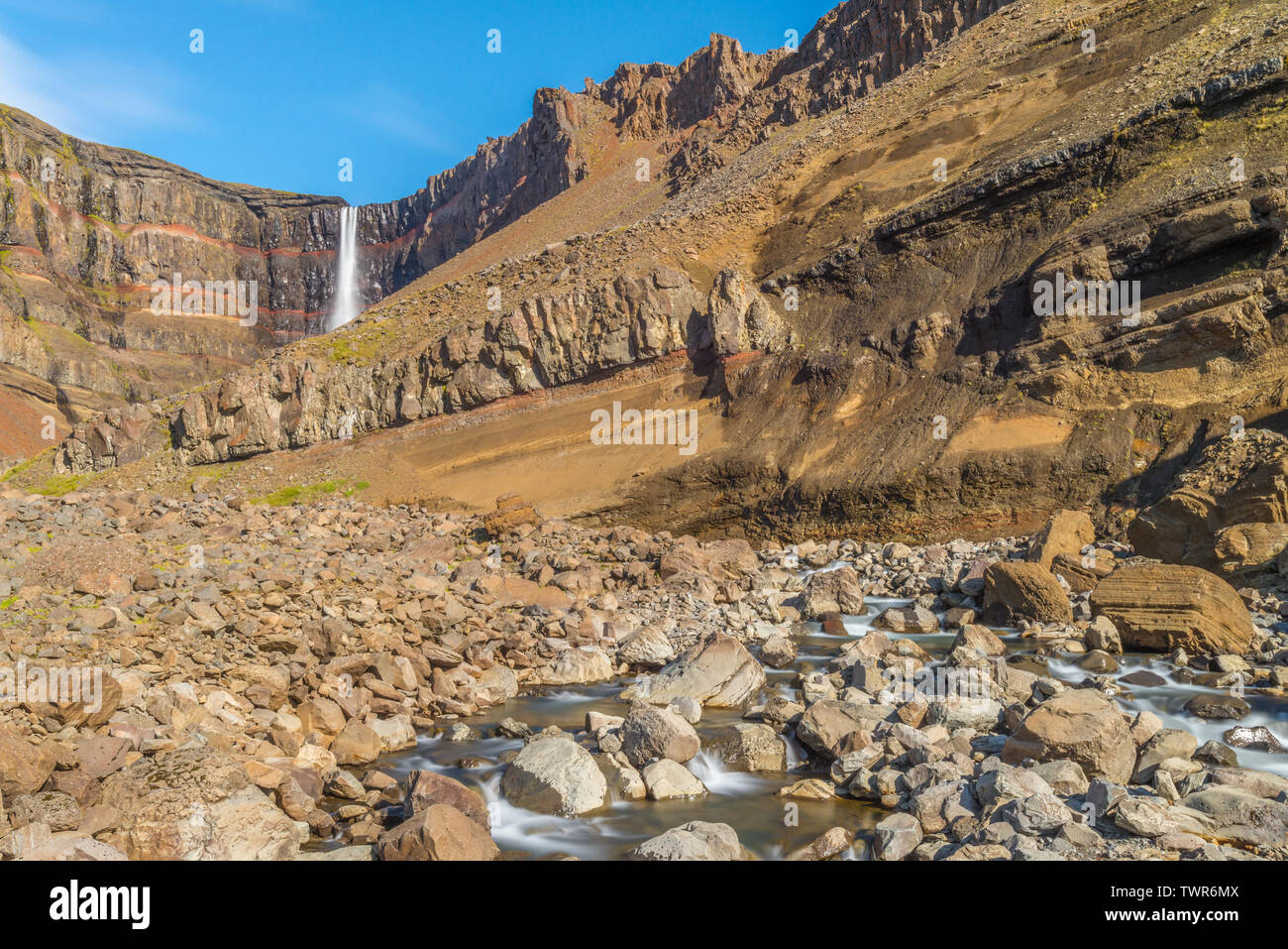 Hengifoss waterfall flowing down the canyon. Rock layers stratified, geological formations seen along the canyon walls. Stock Photo