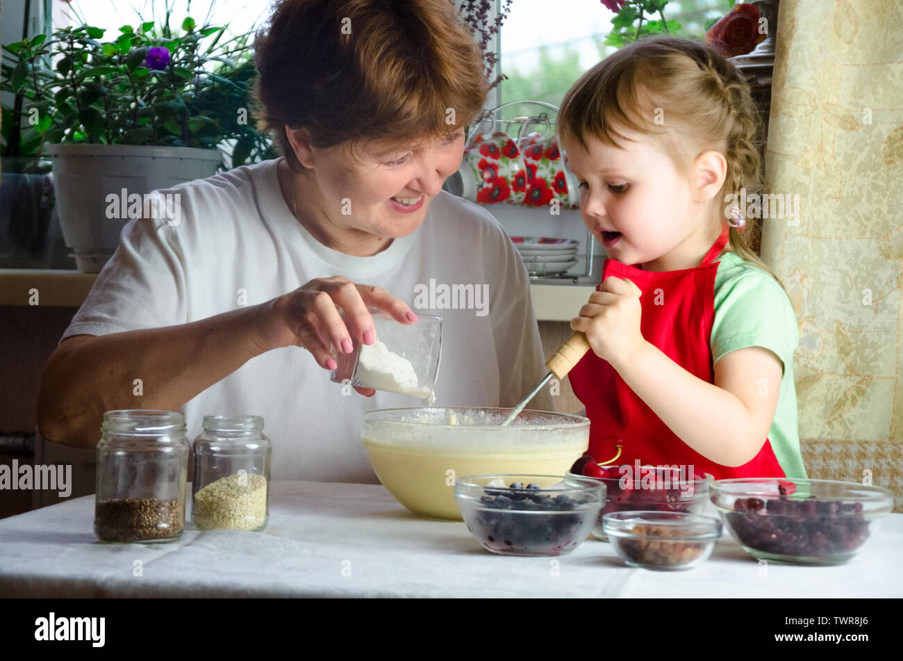 Portrait of faces, hands happy brown-haired granny, granddaughter. toddler girl play with baking, dough, flour on kitchen. child baby try study cookin Stock Photo