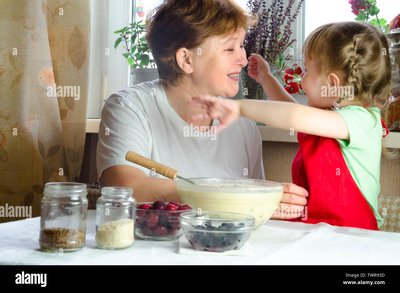 Portrait of faces, hands happy brown-haired granny hug granddaughter. toddler girl play with grandmother on kitchen. child baby hold grandma and laugh Stock Photo