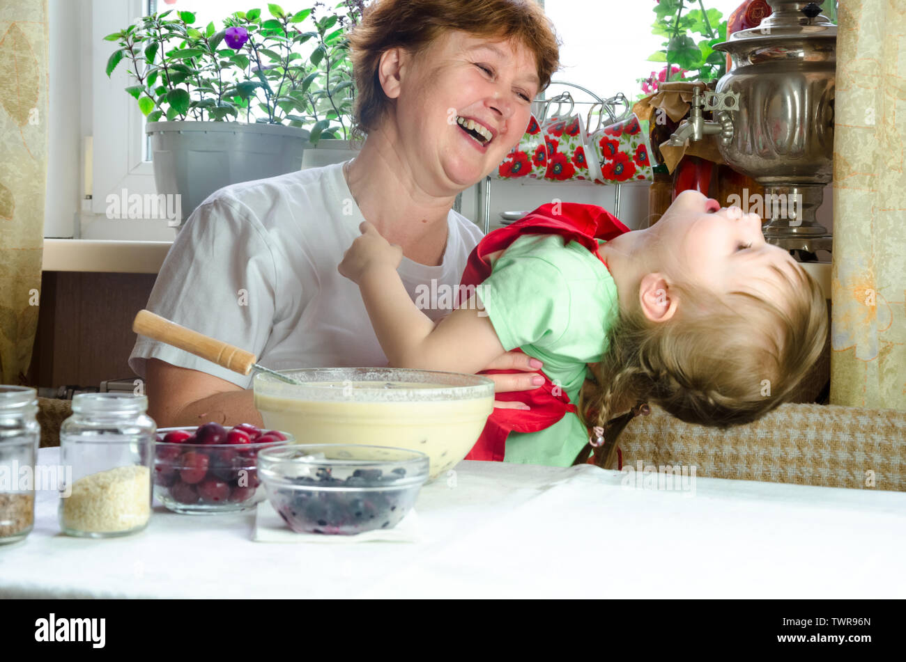 Portrait of faces, hands happy brown-haired granny hug granddaughter. toddler girl play with grandmother on kitchen. child baby hold grandma and laugh Stock Photo