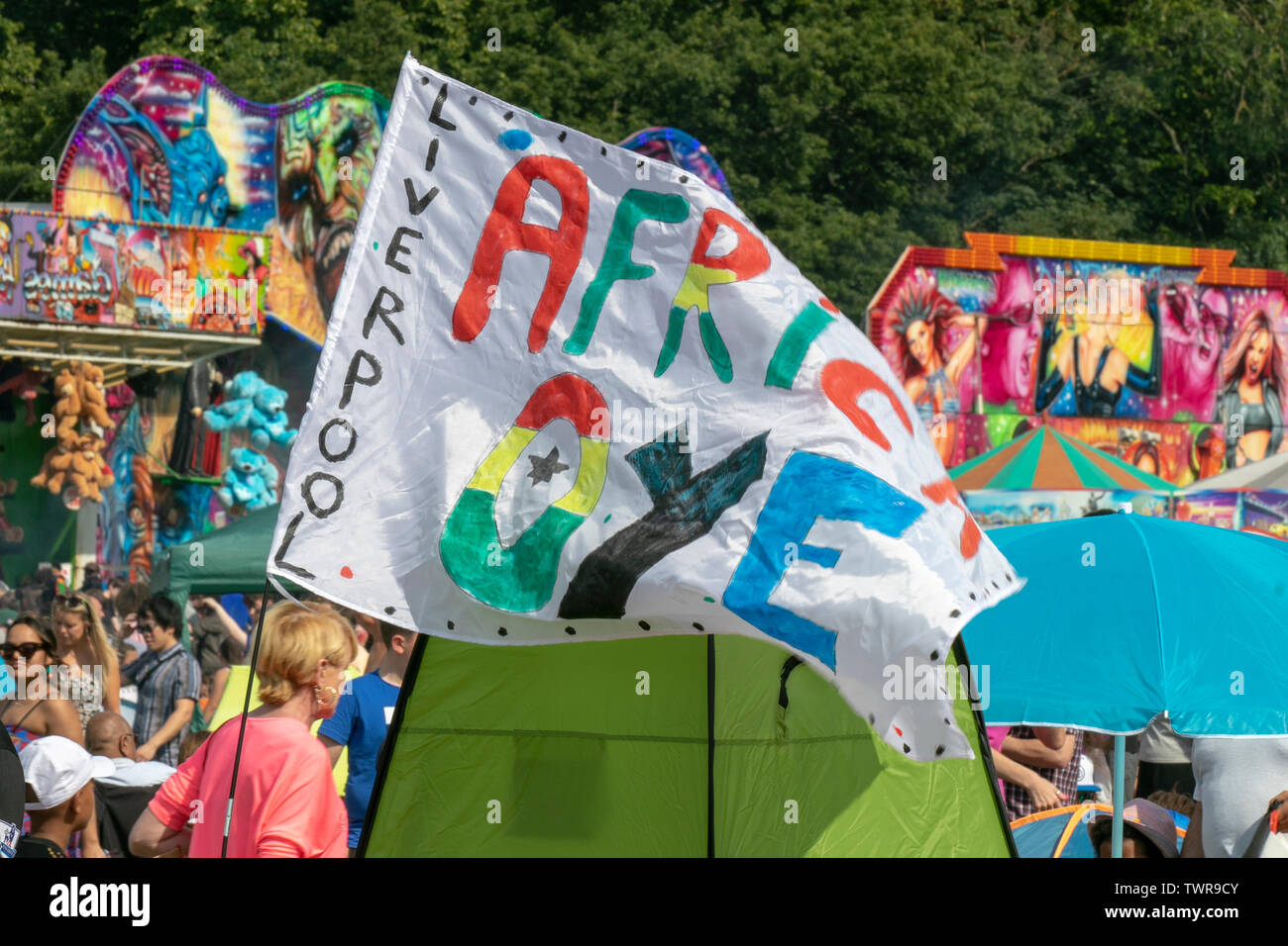 Africa Oye Music Festival banner.  Music lovers, vendors, attend the fantastic Africa Oyé music Festival in Liverpool’s Sefton Park. The UK’s largest free celebration of African music and culture, goods, traders & merchandise brings out the crowds to enjoy the entertainment as festival-goers bask in the sun. Credit: MWI/Alamy Live News Stock Photo