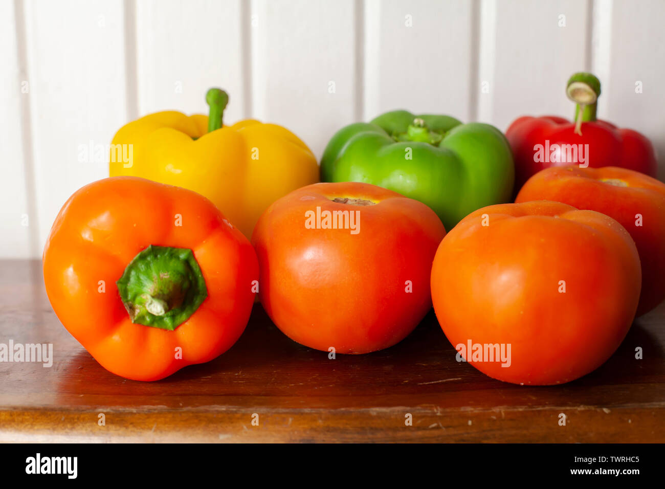 Yellow, green, red, and orange bell peppers with three ripe, red tomatoes Stock Photo