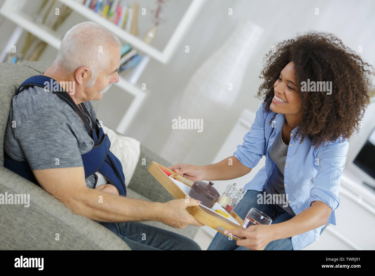carer bringing meal to elderly man with arm injury Stock Photo