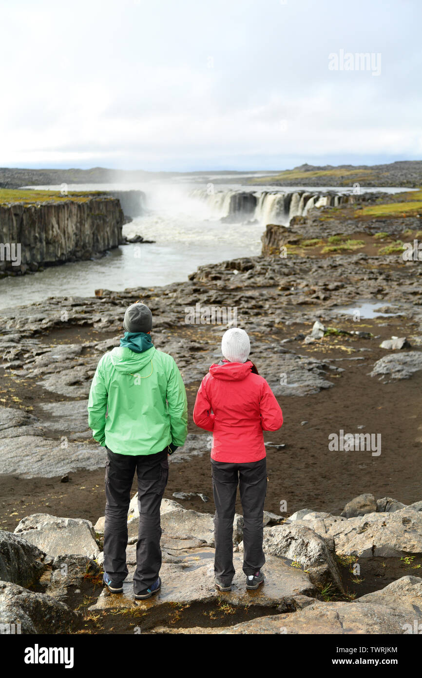 Hikers looking at Iceland nature by waterfall Selfoss waterfall. People enjoying view of famous Icelandic tourist attraction. Hiking couple taking break by Selfoss in Vatnajokull national park. Stock Photo