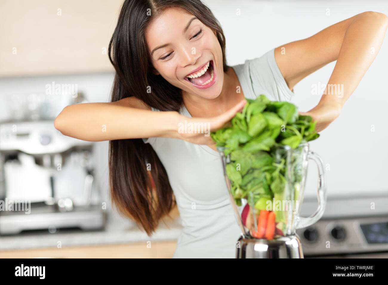 Vegetable smoothie woman making green smoothies with blender home in kitchen. Healthy raw eating lifestyle concept portrait of beautiful young woman preparing drink with spinach, carrots, celery etc. Stock Photo