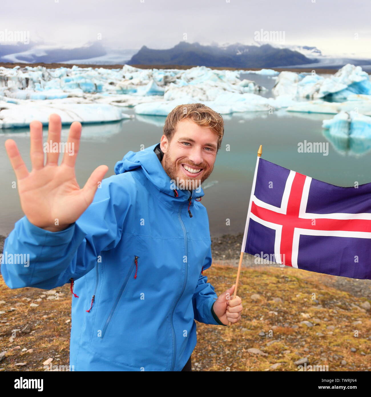 Iceland travel tourist showing Icelandic flag by Jokulsarlon. Man hiker happy holding showing Icelandic flag in front of the glacial lake / glacier lagoon. Happy male smiling in tourism concept. Stock Photo