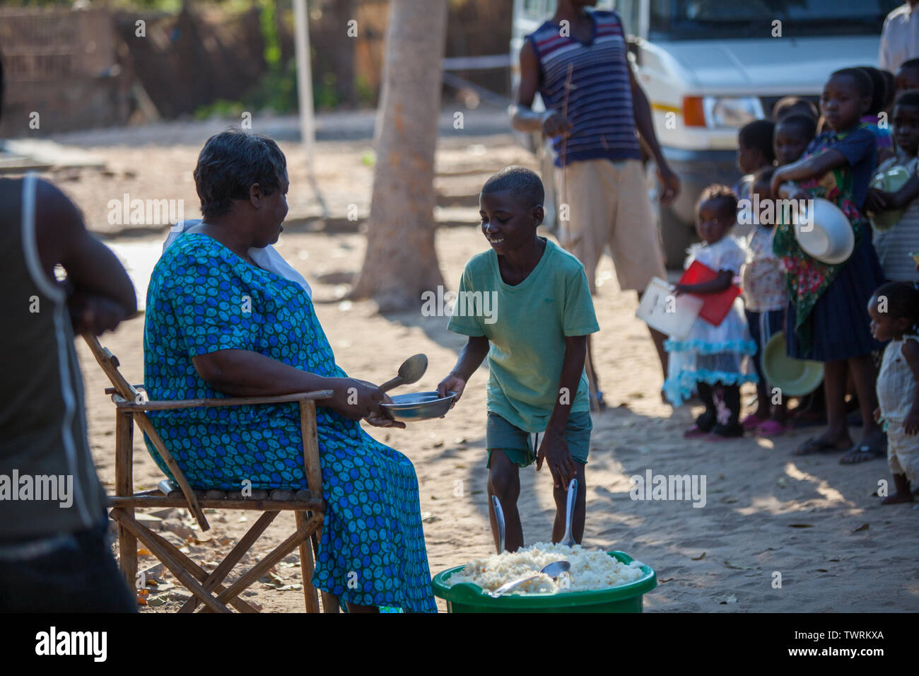 A young boy receiving food from an elderly woman while other children wait in line their turn Stock Photo