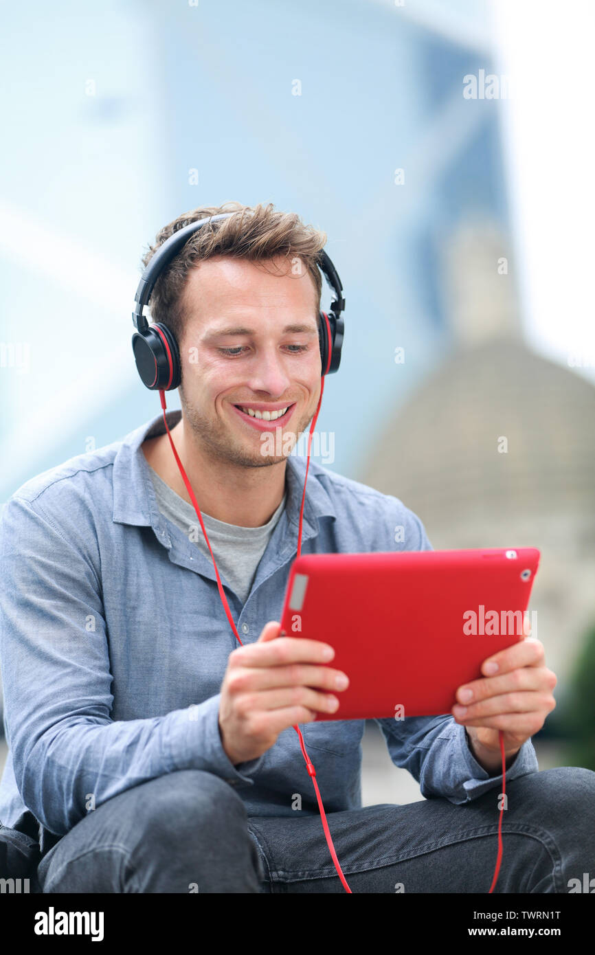 Video chat conversation. Man talking on tablet pc sitting outside using app on 4g wireless device wearing headphones. Casual young urban professional male in his late 20s. Stock Photo