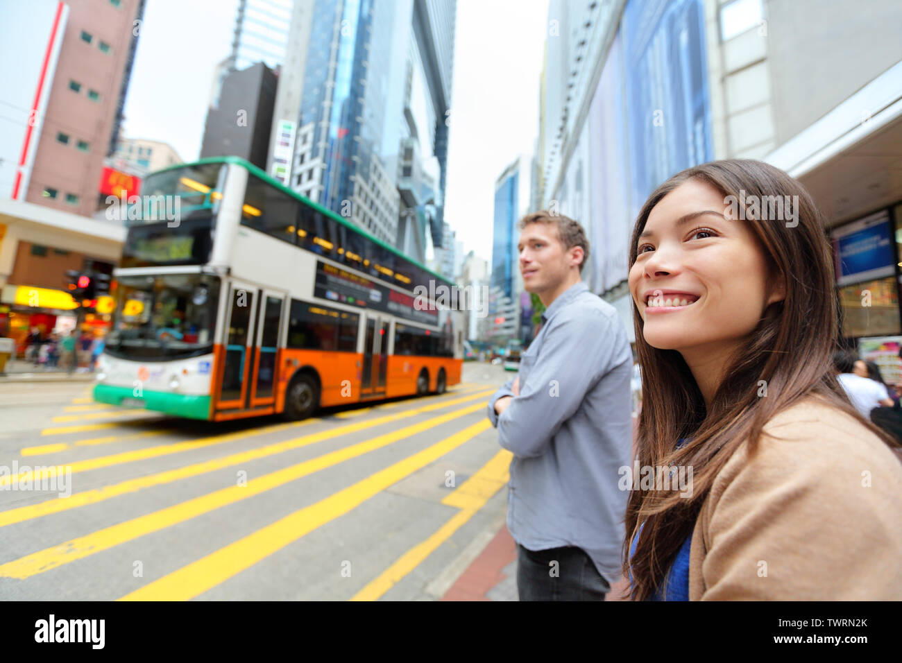 Hong Kong People walking in Causeway Bay crossing busy road with double decker bus. Urban mixed race Asian Chinese / Caucasian woman smiling happy living in city. Stock Photo