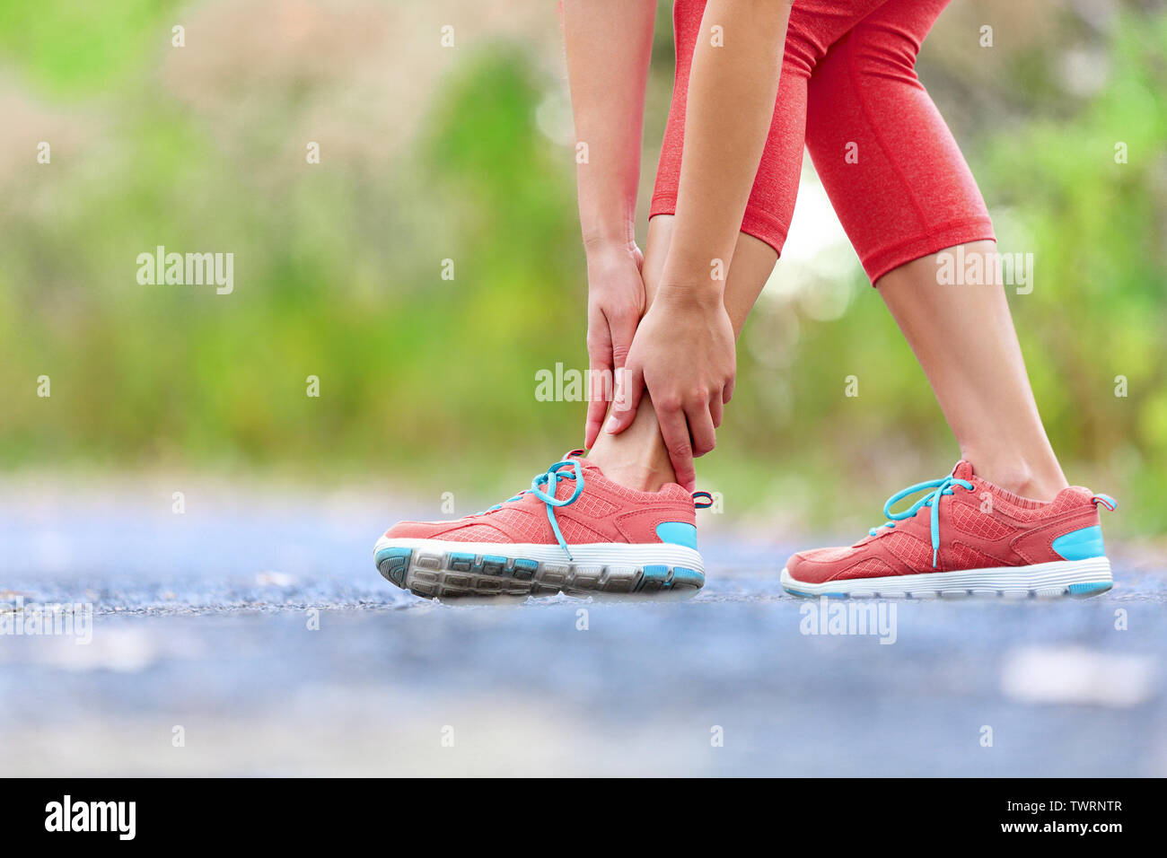 Twisted broken ankle - running sport injury. Female runner touching foot in pain due to sprained ankle. Stock Photo