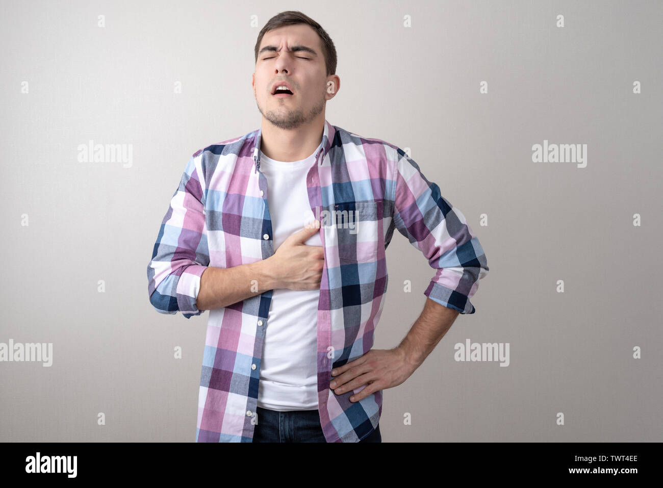 Portrait of a sickly man holding his heart on a gray background. heart disease Stock Photo
