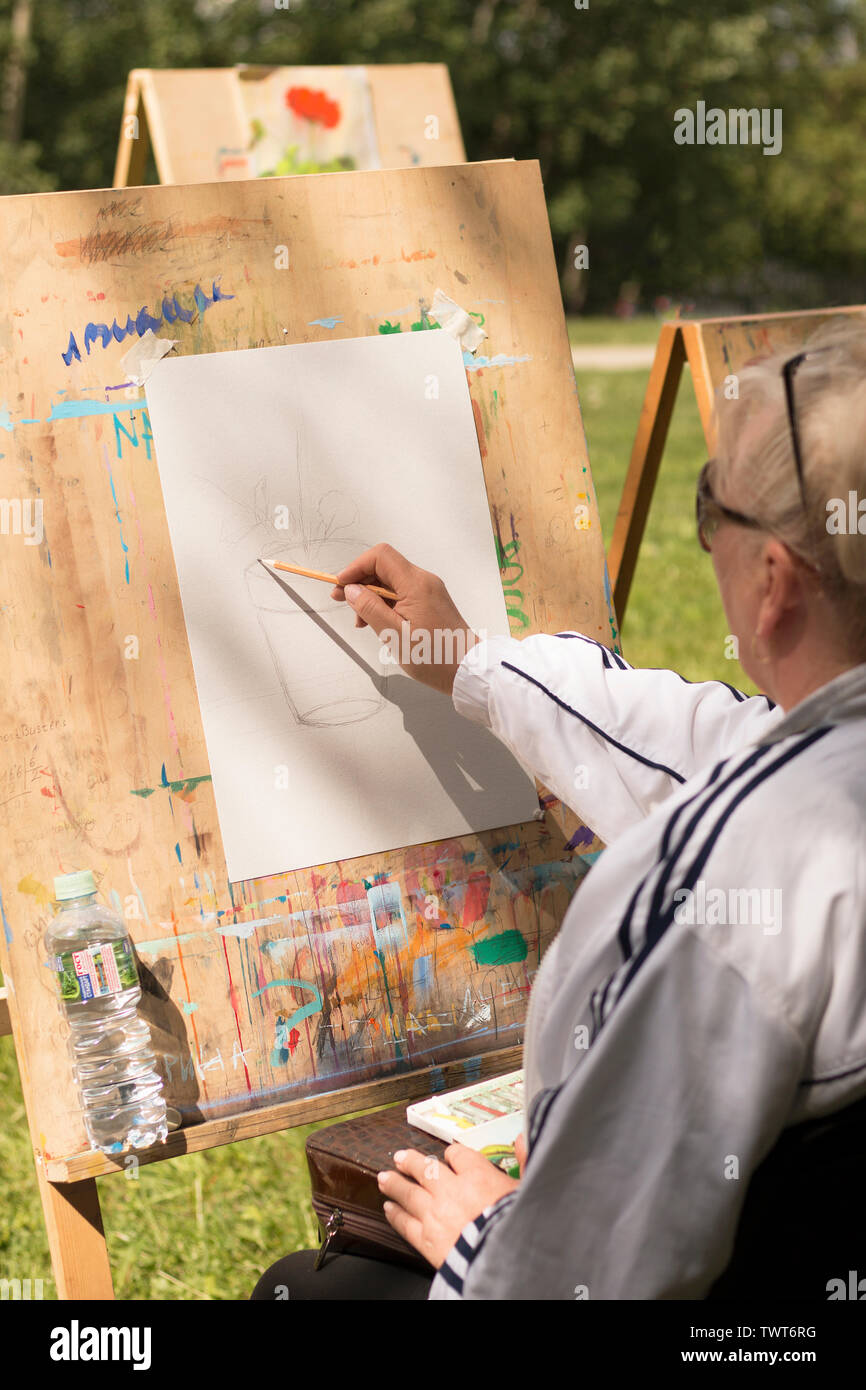 Mature grey-haired woman draws floral sketch outdoors in art studio in sunny day. Moscow - June 1, 2019. Hobby for retired people, social programs for Stock Photo