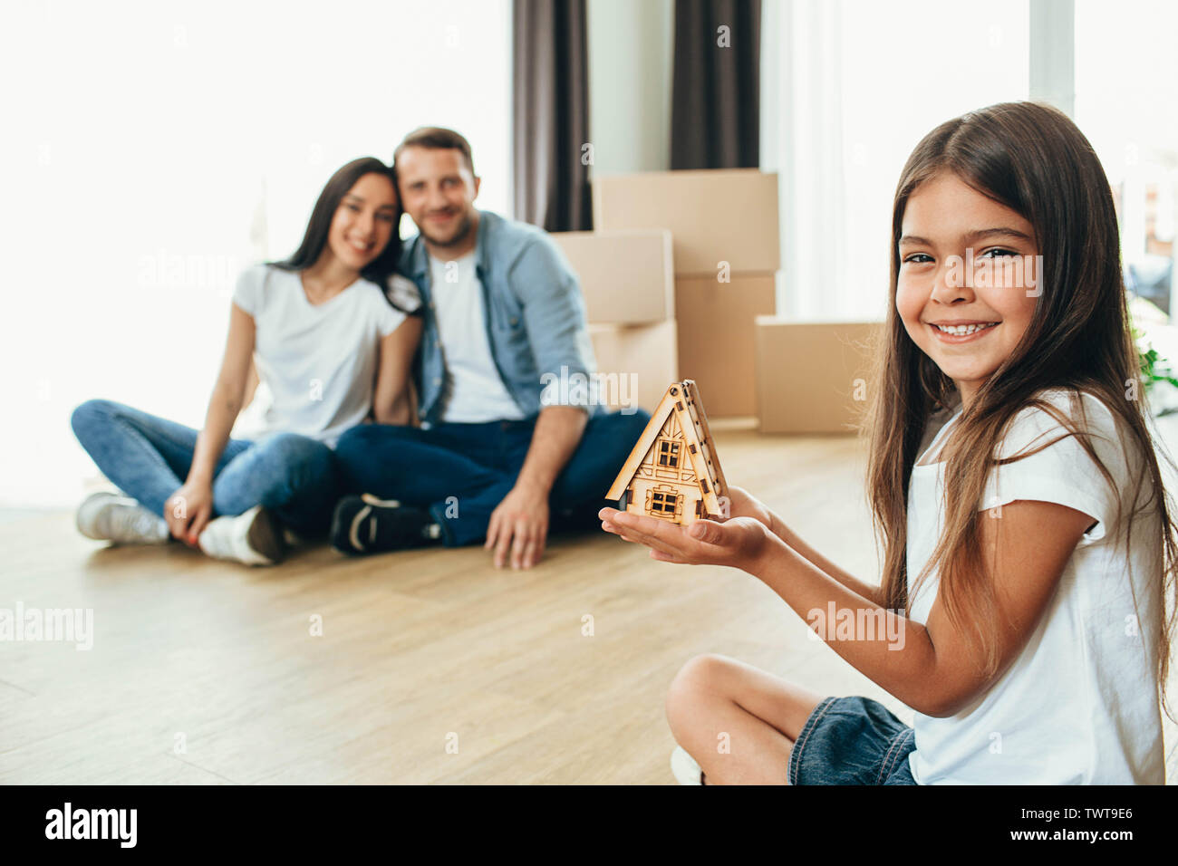 happy child holding little miniature house, after her sitting her happy parents into their new house. Buying new apartment Stock Photo