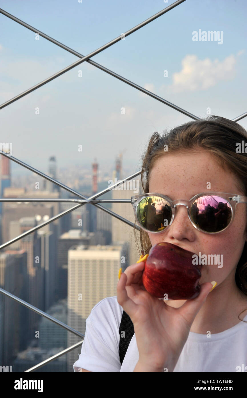child biting into a big red apple on top of the Empire State Building New York Stock Photo