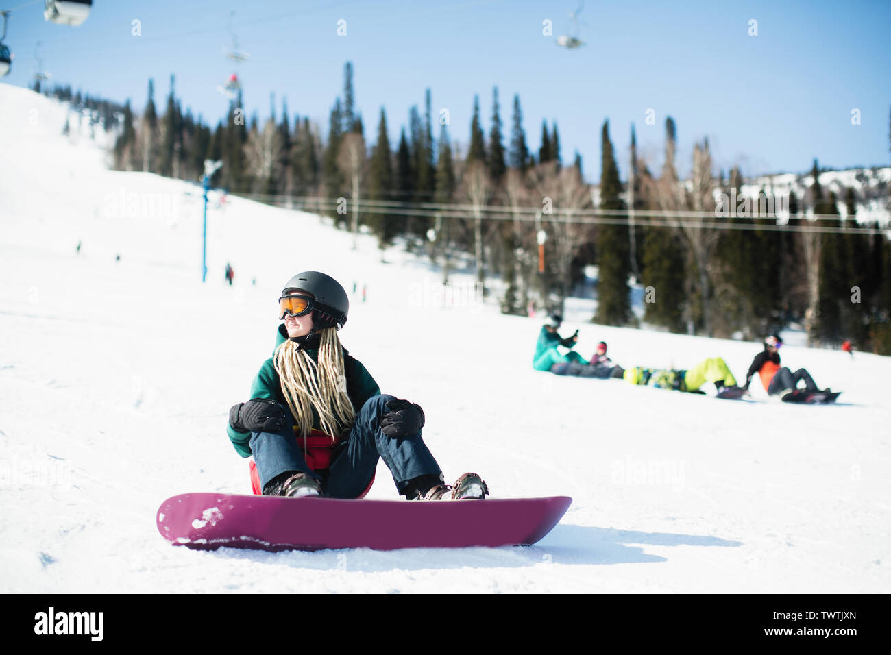 Woman snowboarder sitting on a snowy slope. Stock Photo