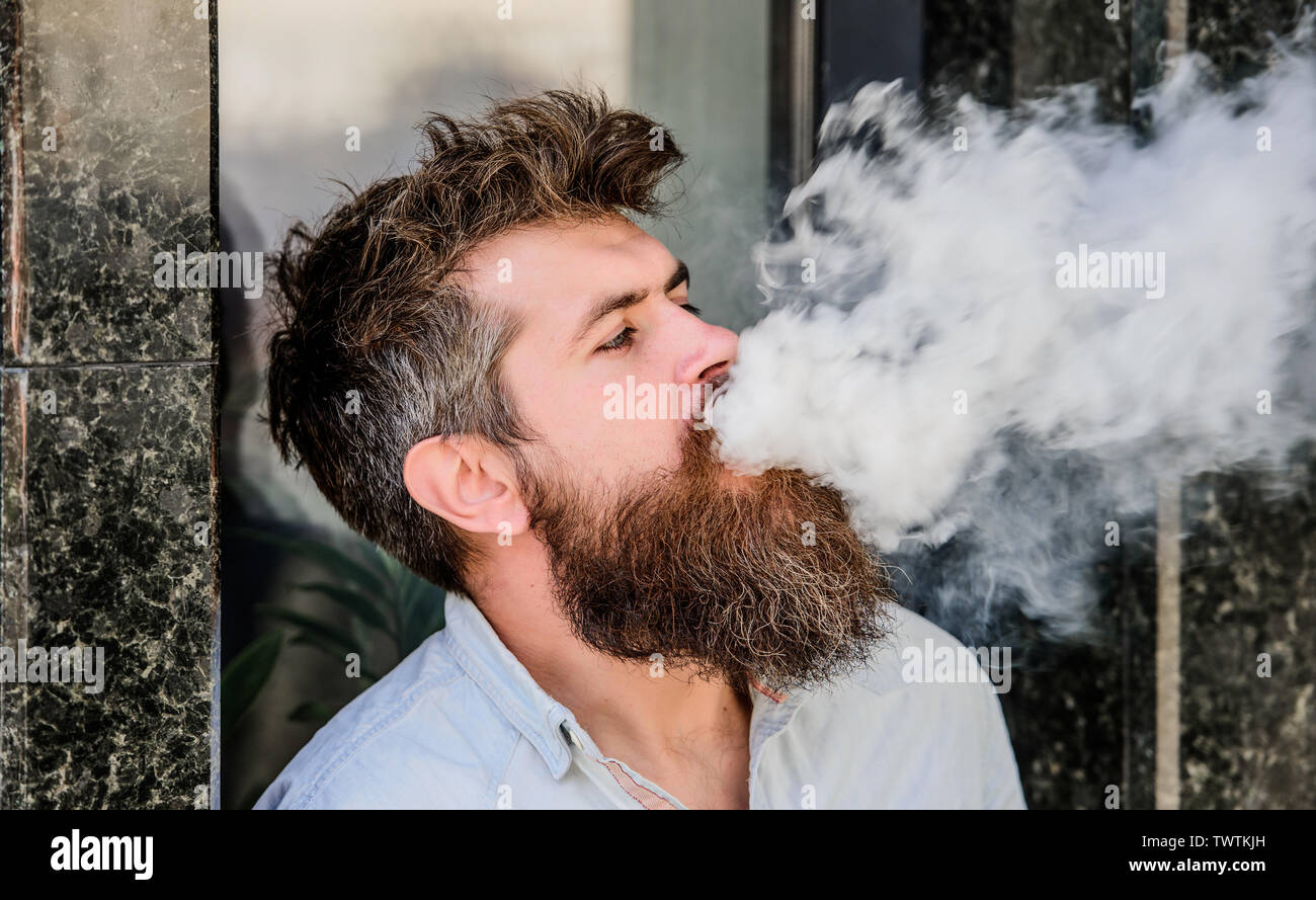 Smoking electronic cigarette. Stress relief concept. Smoking device. Man  long beard relaxed with smoking habit. Clouds of flavored smoke. Bearded man  smoking vape. Man with beard breathe out smoke Stock Photo -