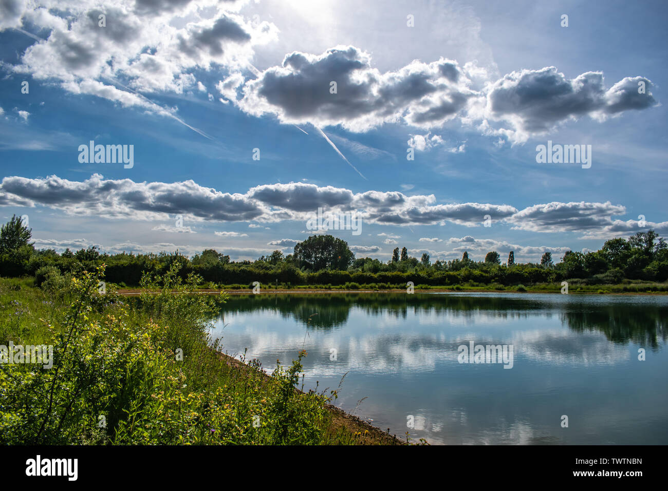 The cloudy sky above is reflected in the still waters of a lake below. Taken in Oxfordshire, England. Stock Photo