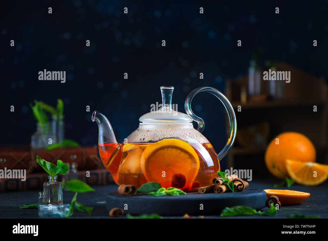 Citrus tea header with cinnamon and mint leaves in a glass teapot, dark food photography with copy space. Stock Photo