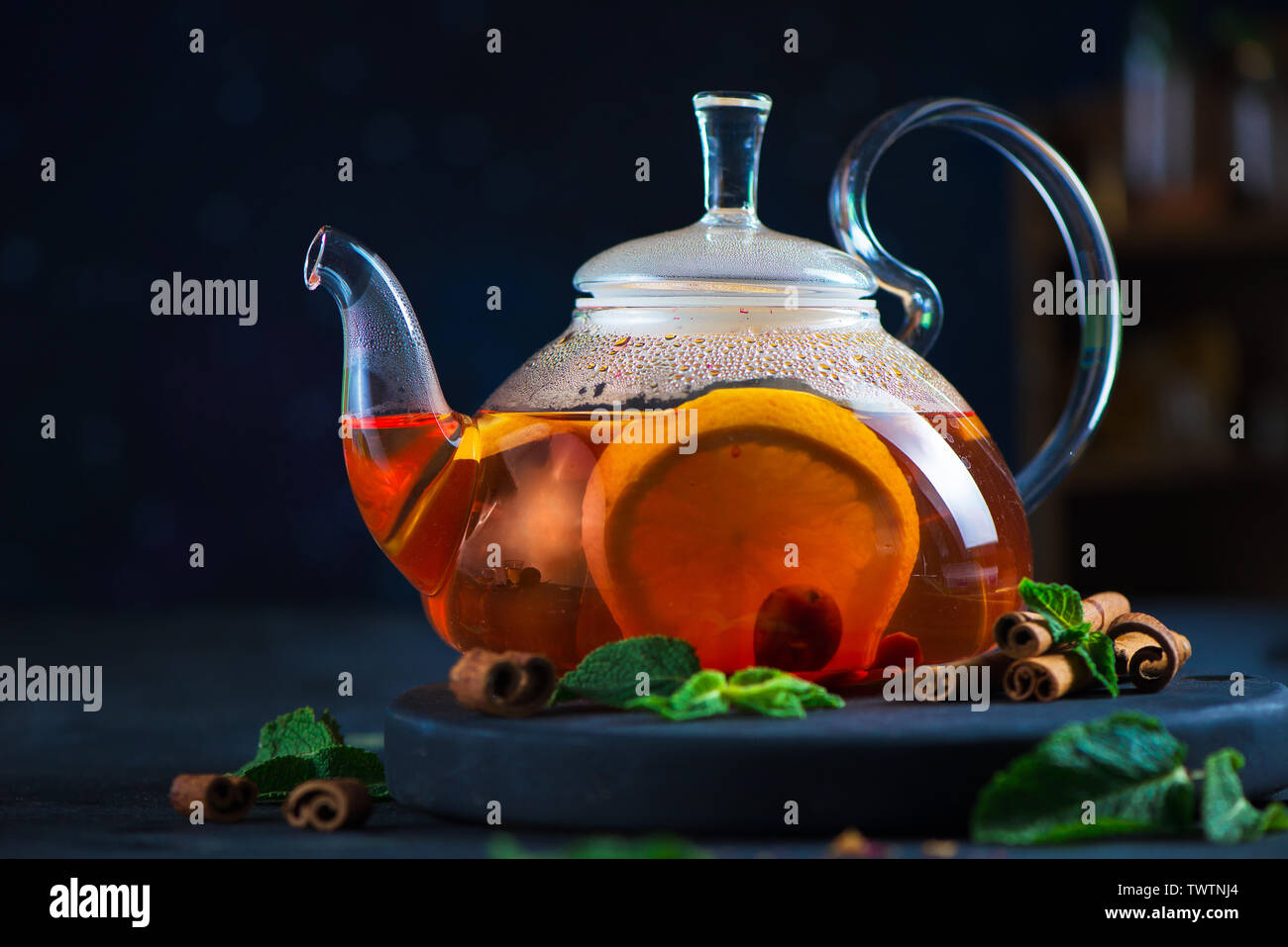 Citrus tea header with cinnamon and mint leaves in a glass teapot, dark food photography with copy space. Stock Photo