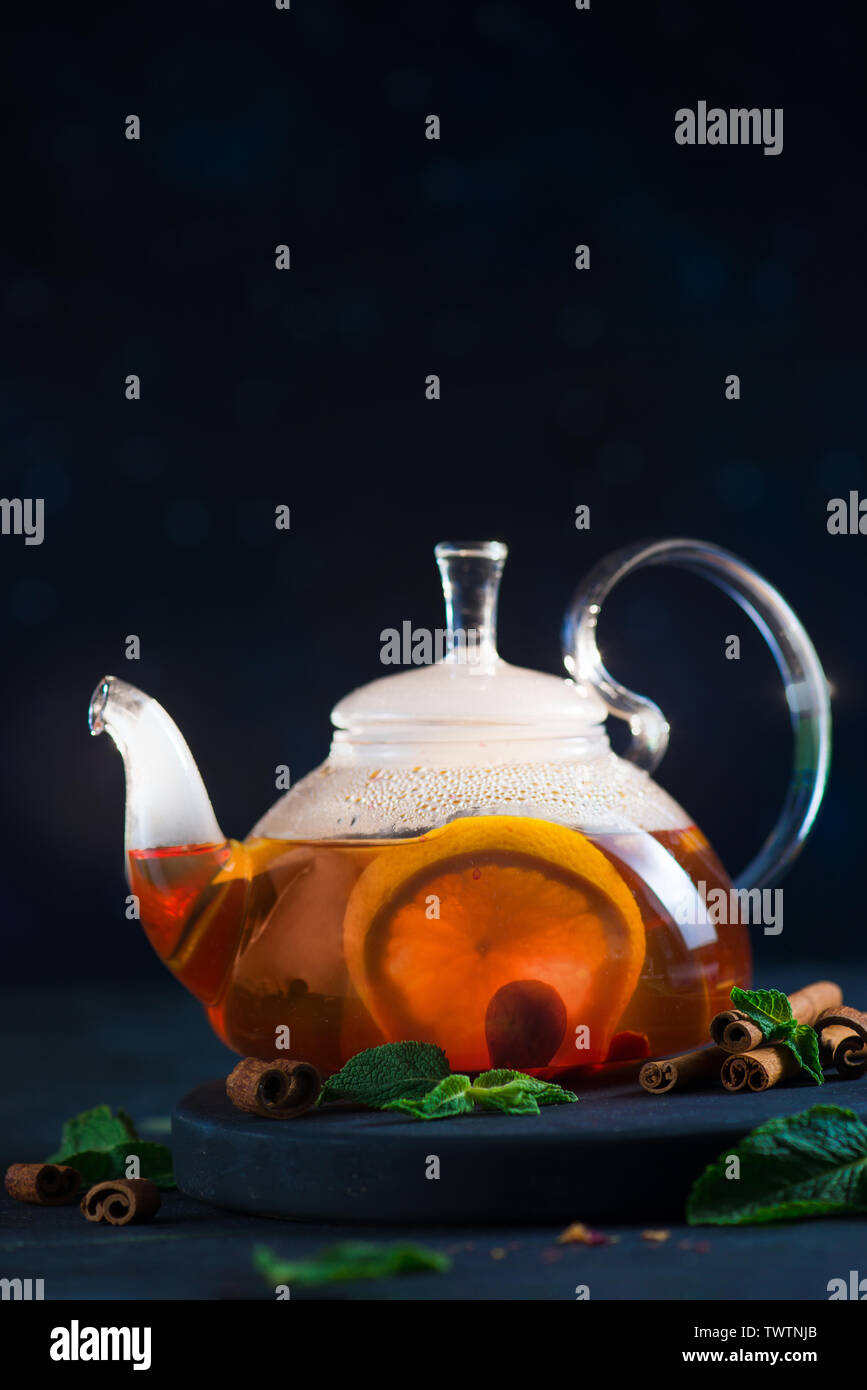 Close-up of citrus tea with cinnamon and mint leaves in a glass teapot, dark food photography with copy space. Stock Photo