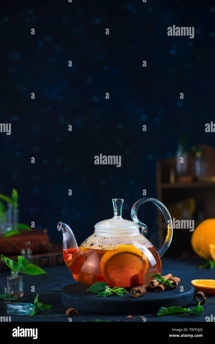 Citrus tea with cinnamon and mint leaves in a glass teapot, dark food photography with copy space. Stock Photo