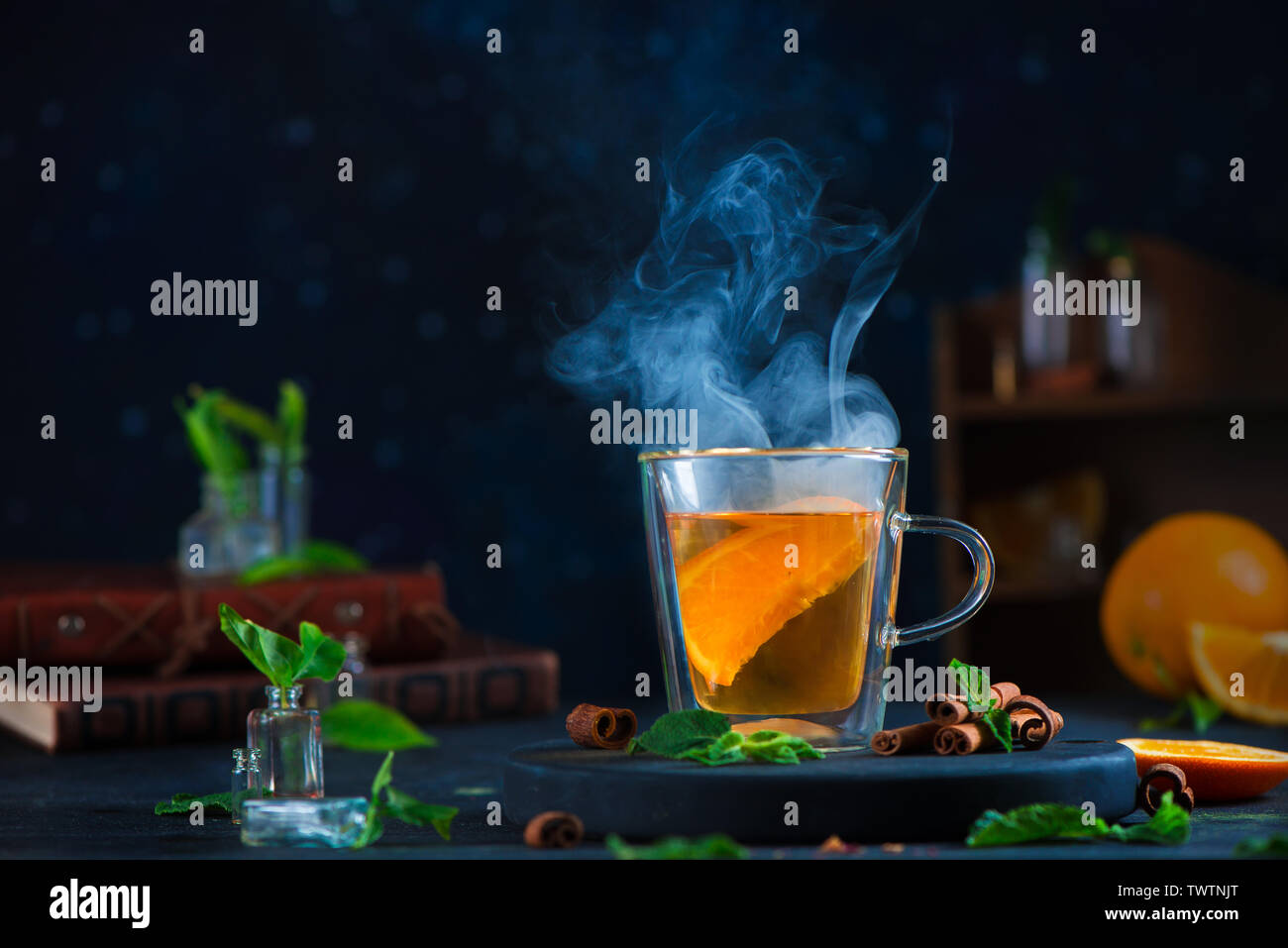 Double wall glass cup with citrus tea, cinnamon, and mint leaves. Steam in dark food photography with copy space. Stock Photo