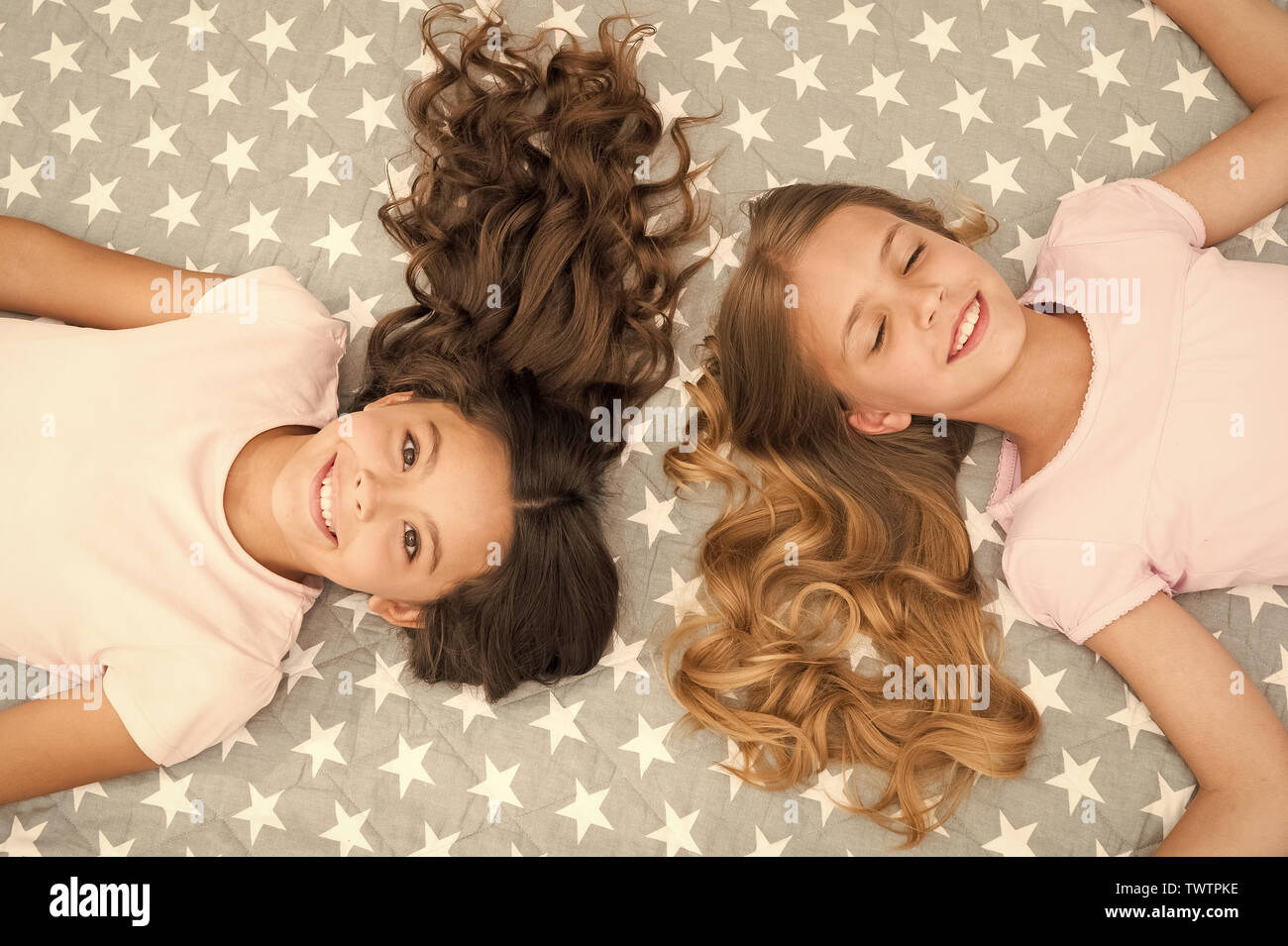 Girls with long curly hair lay on bed top view. Children perfect curly  hairstyle looks cute. Conditioner mask organic oil keep hair shiny and  healthy. Amazing curls tips. Make it curly but