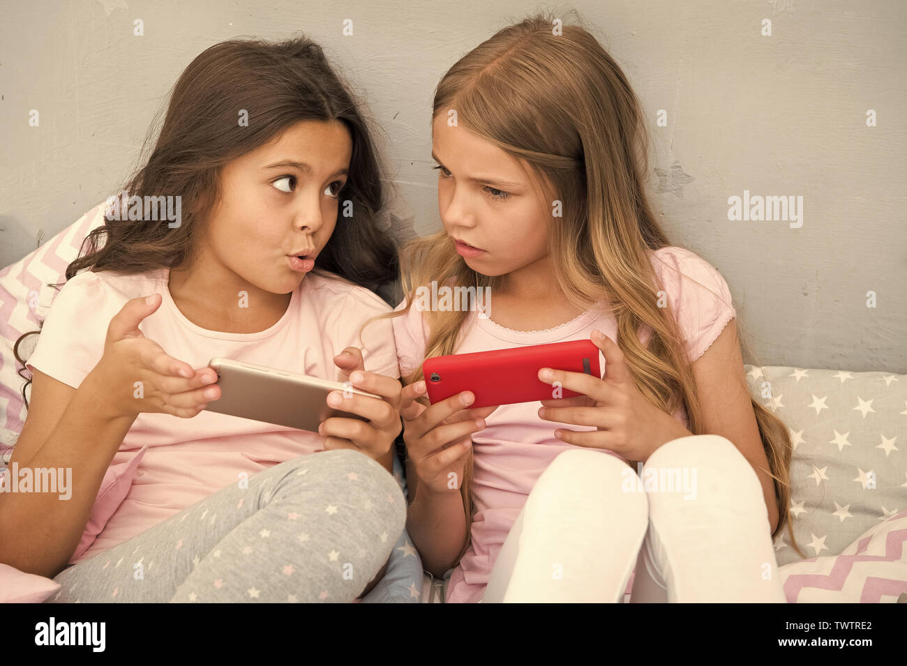 Kids play smartphone mobile game application. Smartphone application concept. Girlish leisure pajama party. Girls smartphone little bloggers. Explore social network. Smartphone for entertainment. Stock Photo