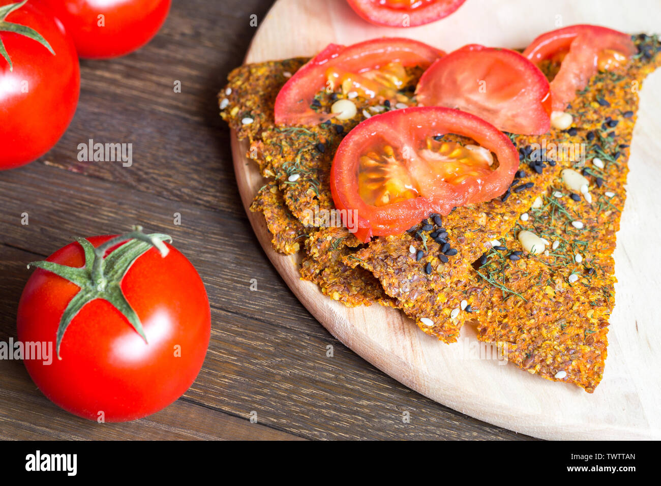 Delicious vegan crisp bread with tomatoes on wooden background. Fast raw diet snack. Close-up. Selective focus on foreground. Top angle view. Healthy Stock Photo