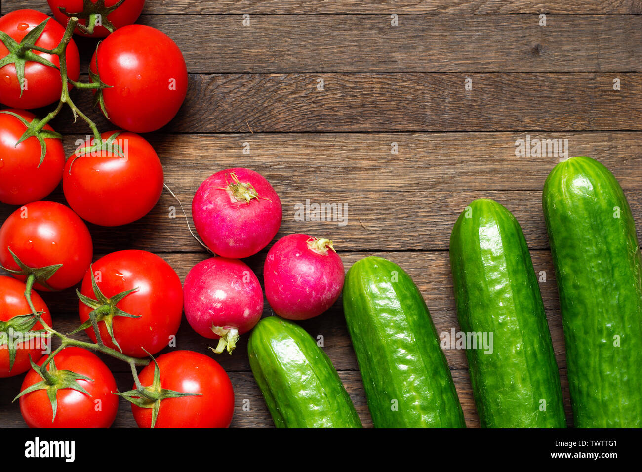 Green cucumbers with red ripe tomatoes and radishes on wooden desk. Top view. Copy space. Water drops on washed vegetables. Fresh raw food. Agricultur Stock Photo