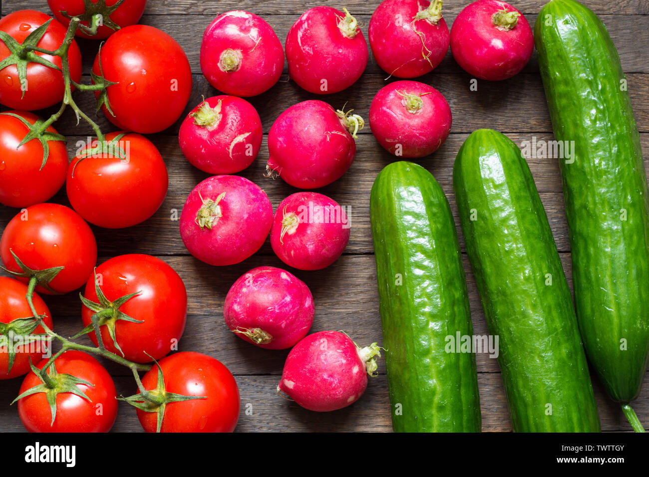 Agriculture background. Tomatoes, radishes and cucumbers on table. Fresh raw food. Water drops on washed vegetables. Close up. Top view. Stock Photo