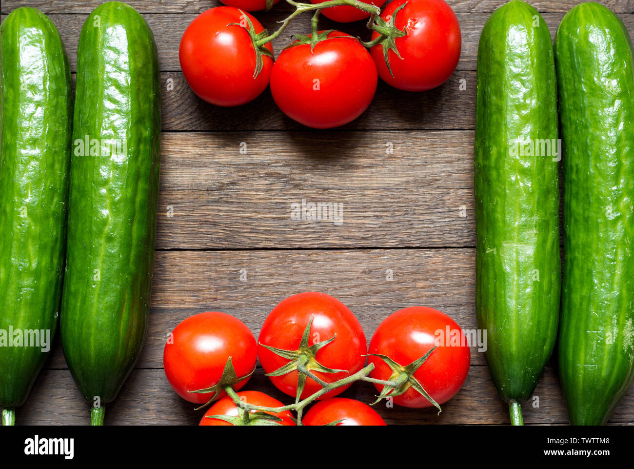 Vegetables background with copy space in center. Red tomatoes on top and bottom and green cucumbers by sides. Agriculture. Healthy meal concept. Top v Stock Photo