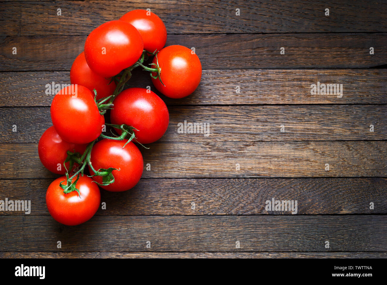 Fresh red tomatoes on branch on dark brown wooden table. Copy space ...
