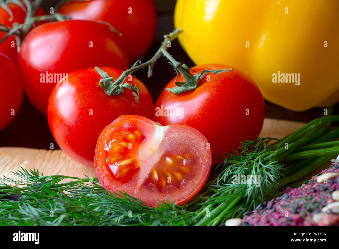 Ripe red slice of tomato with green dill and sweet yellow pepper on kitchen board. Close up. Healthy nutrition concept. Raw foods. Stock Photo