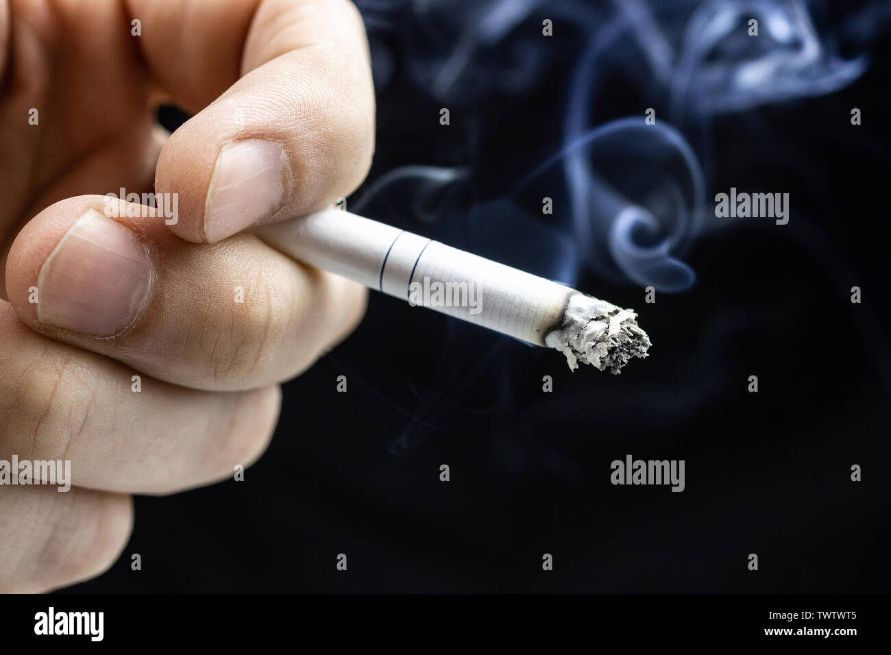 cigarette smell on hands Hand with cigarette. White burning cigarette in the hands of a male smoker  on a dense black background with smoke. isolated on black background. Ashes  Stock Photo