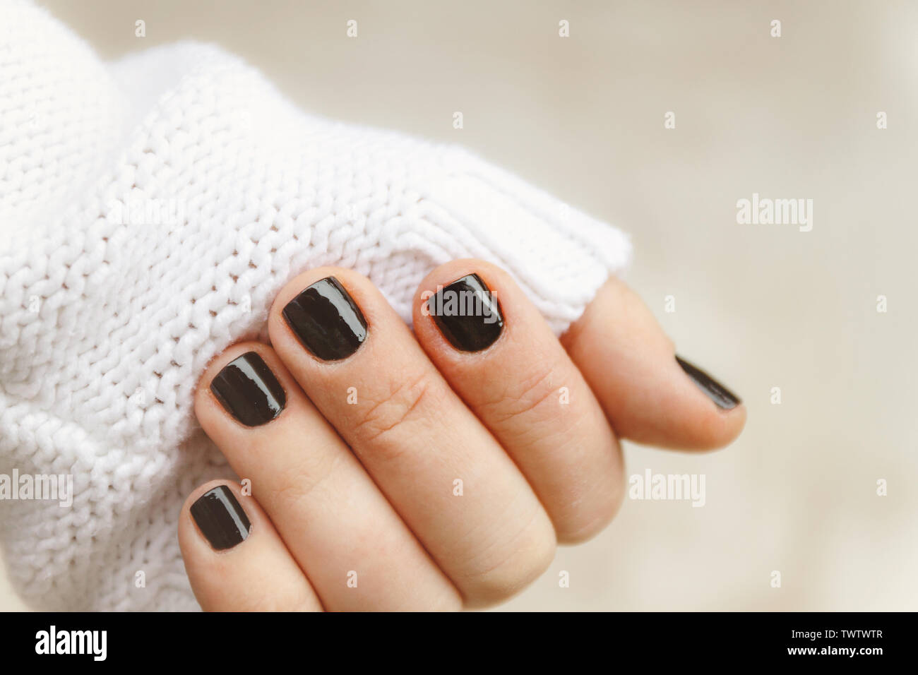 hand with black manicure on short nails in a white sweater on a light  background. The concept of a stylish and warm winter Stock Photo - Alamy