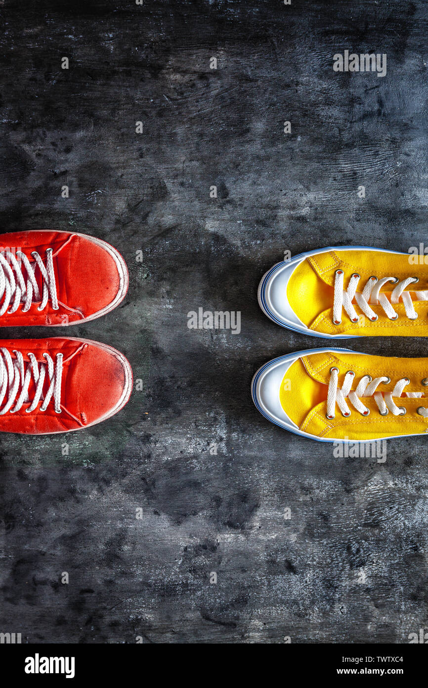 red, old, worn, dirty, torn, sneakers, and new yellow sneakers against a dark grunge background. view from above. Copy space. Stock Photo
