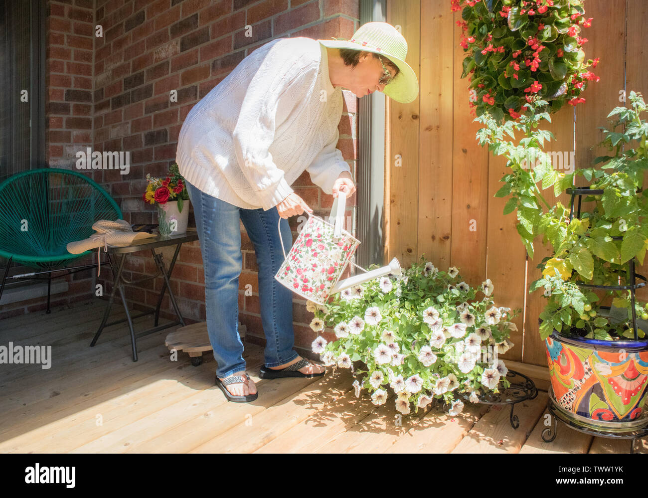 A mature lady watering her flowers and plants on her tiny patio. Stock Photo
