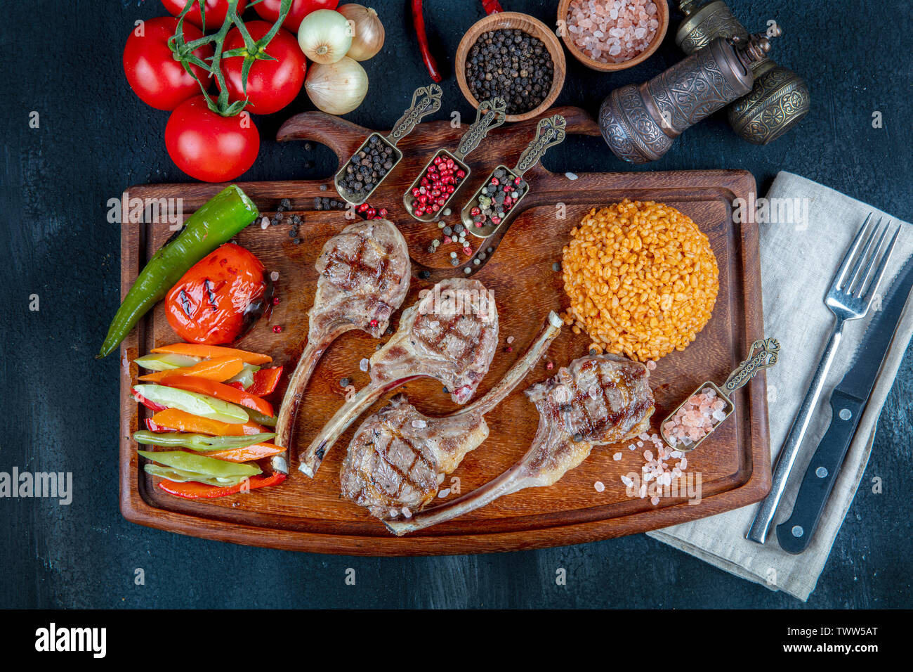 Lamb ribs grilled on cutting board with roasted vegetables. Top view Copy space Wooden background. Halal restaurant concept. Stock Photo